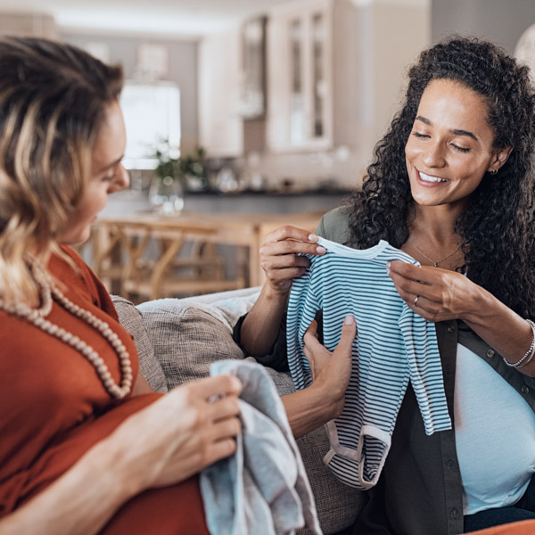 Happy pregnant friends looking baby clothes